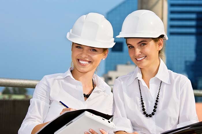 Two construction women wearing hard hats laughing holding clipboards registering new workers