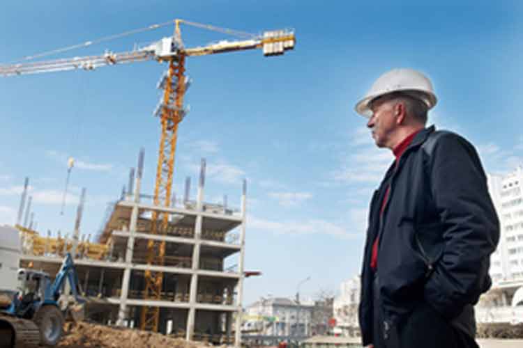 Construction worker wearing a hard hat stood looking at a building in construction with a crane in the middle