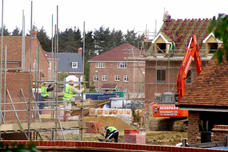 Construction housing site showing workers on scaffolding on the side of a building