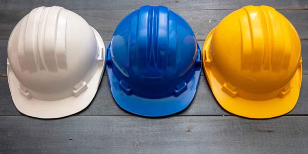 Three construction hard hats, white blue and yellow set on a wood floor.