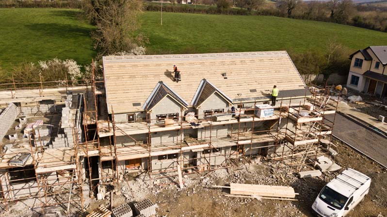 Construction housing site showing workers building a roof and a wall with high vis and hard hats on