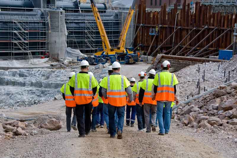 Construction worker gang with yellow and orange high visibility clothing and a hard hat walking on a construction site