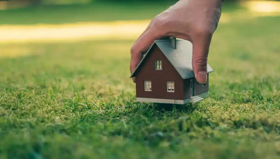 Hand lowering a house into a grass field with the text the rise of prefabricated construction advantages and challenges for southwest builders