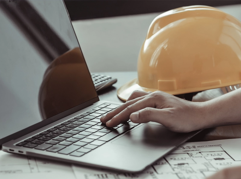 Builders helmet resting on an open laptop showing a hand typing