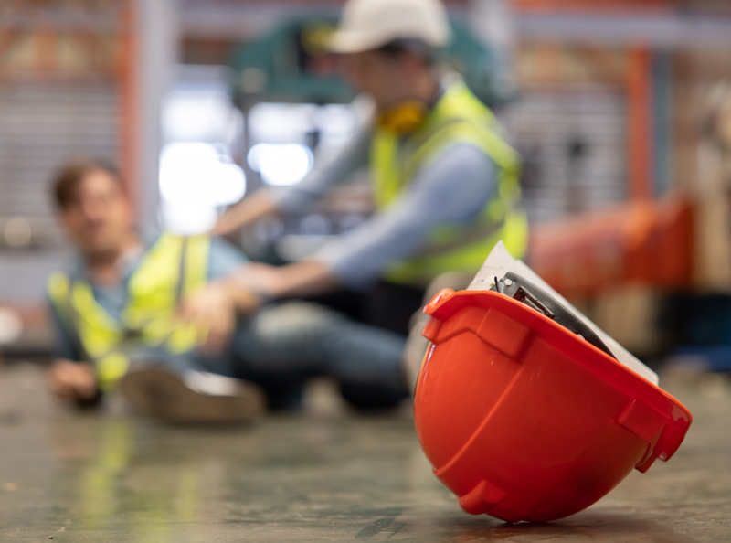 Construction worker fallen on the floor with a hard hat in the foreground
