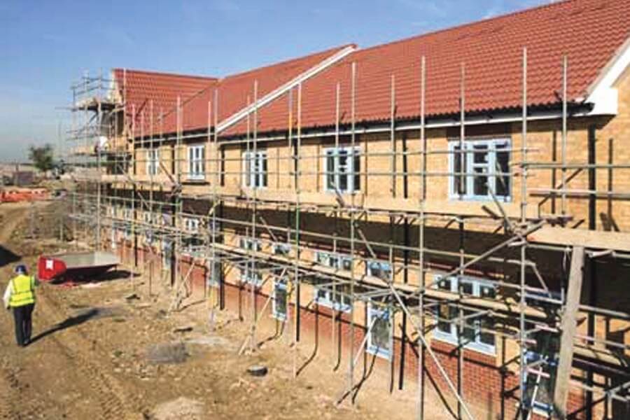 Construction site showing a row of terraced houses with scaffolding and a workman walking past