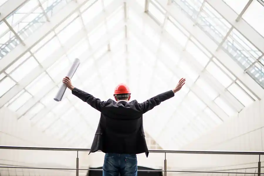 Construction worker jumping in the air in happiness with a high visibility vest and work gear with the title of the blog to the left