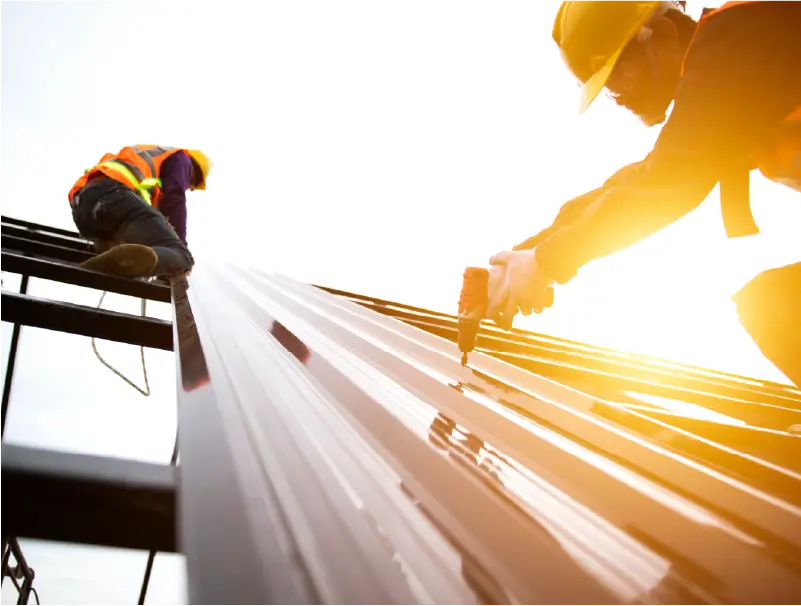 Construction workers laying roofing sheet on a roof holding tools for the job in a tough labour shortage