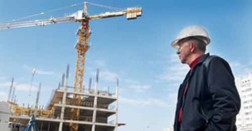 Construction worker wearing a hard hat stood looking at a building in construction with a crane in the middle