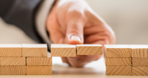 Building blocks to the right and left with a person holding a bridge of blocks between symbolising the gap that is bridged by construction recruitment agencies during labour shortages