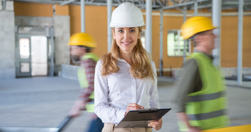 Construction Inclusion Coalition Lady with a white hard hat and clipboard with a blurred construction background with two workmen