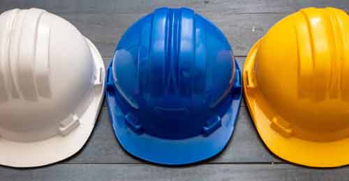 Three construction hard hats, white blue and yellow set on a wood floor.