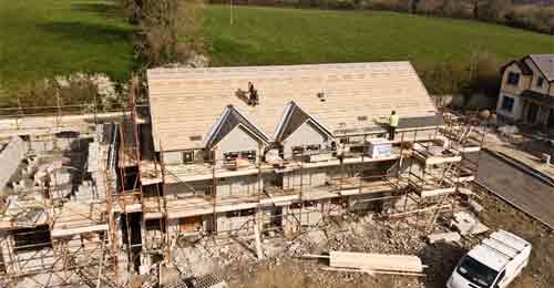 Construction housing site showing workers building a roof and a wall with high vis and hard hats on