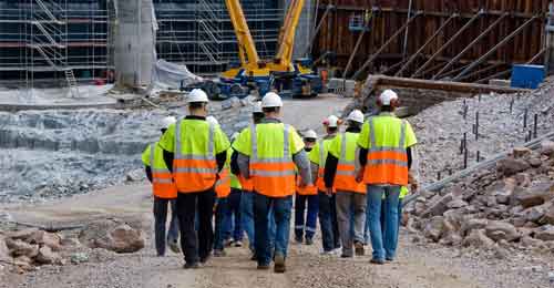 Construction worker gang with yellow and orange high visibility clothing and a hard hat walking on a construction site