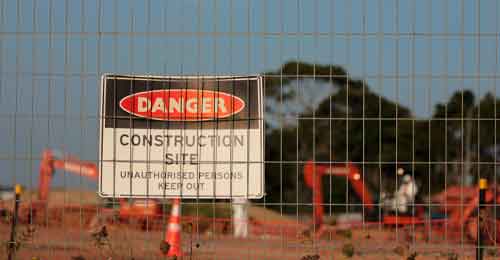 A large sign reading Danger Construction site unauthorised persons keep out taken through a fence showing construction site machinery
