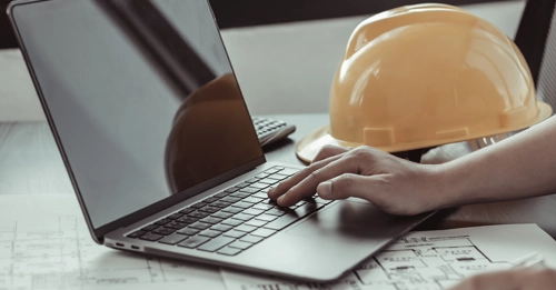 Builders helmet resting on an open laptop showing a hand typing