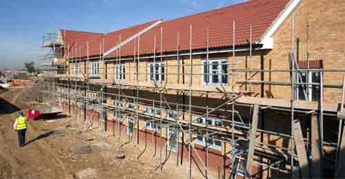 Construction site showing a row of terraced houses with scaffolding and a workman walking past