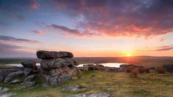A view of Bodmin moor showing the sunset from the top of a hill with boulders in view